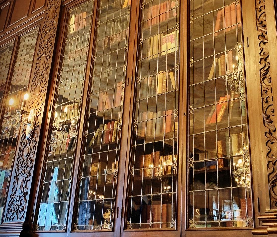 glass book case with old books inside wood panel walls with sconce surround